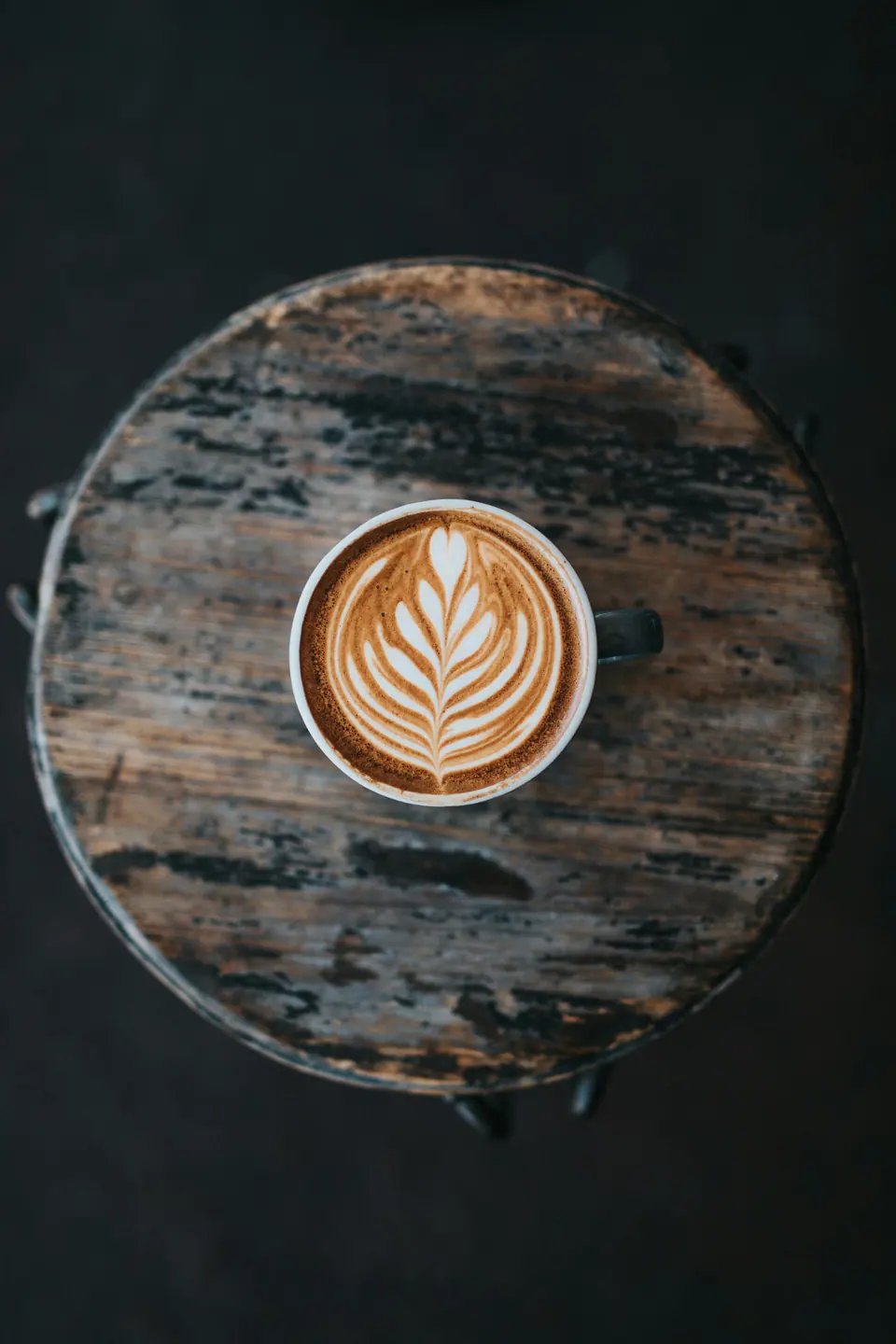 Professionally photographed latte with leaf-pattern latte art on a wooden table